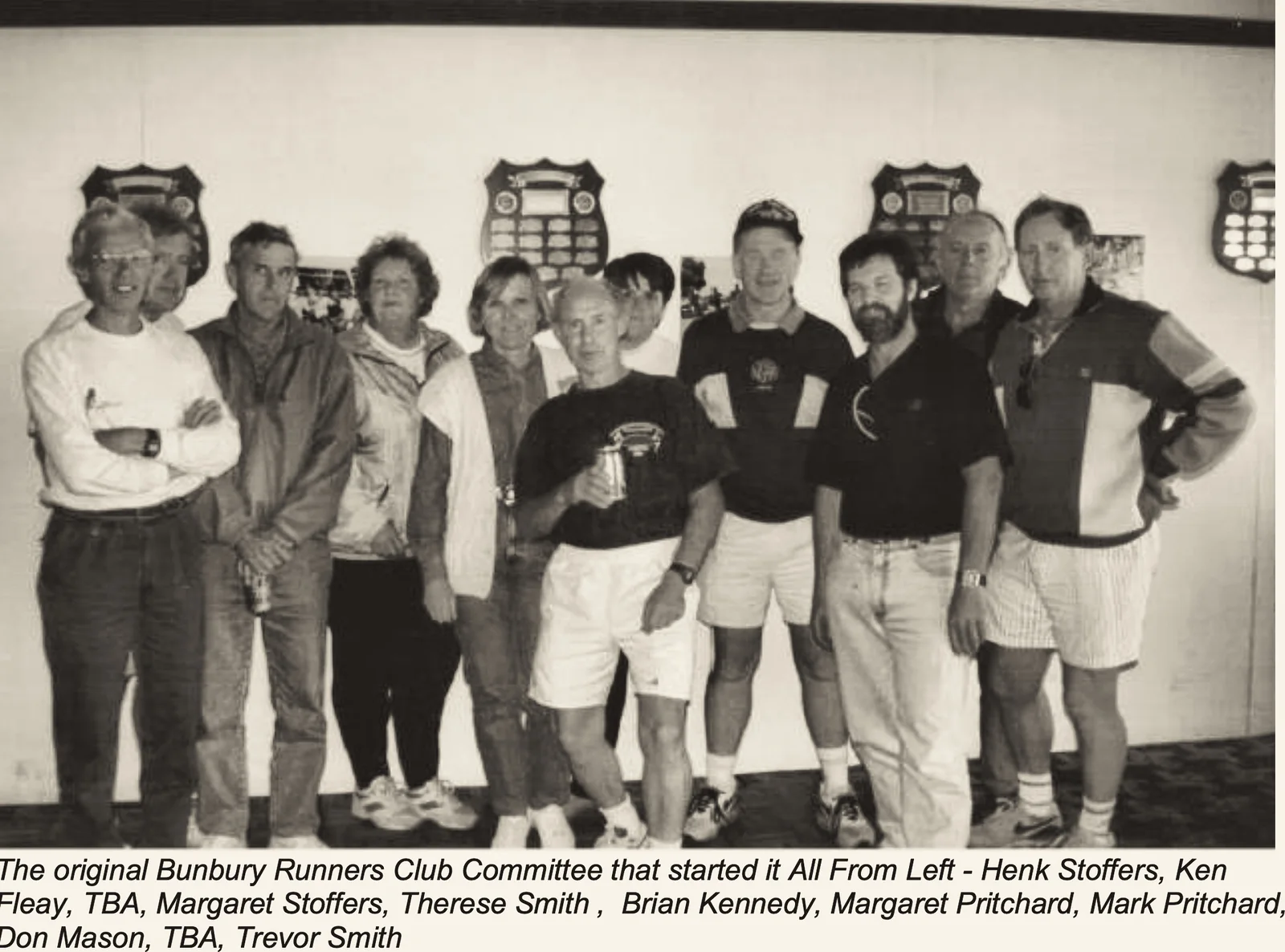 A group portrait of the original Bunbury Runners Club committee standing in the clubrooms, with a printed caption naming them.