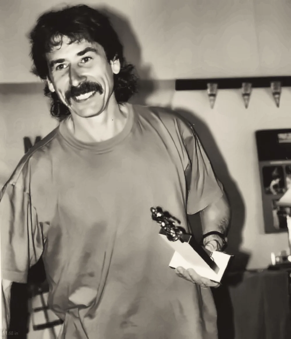 A runner holding a trophy and an envelope at an indoor presentation.