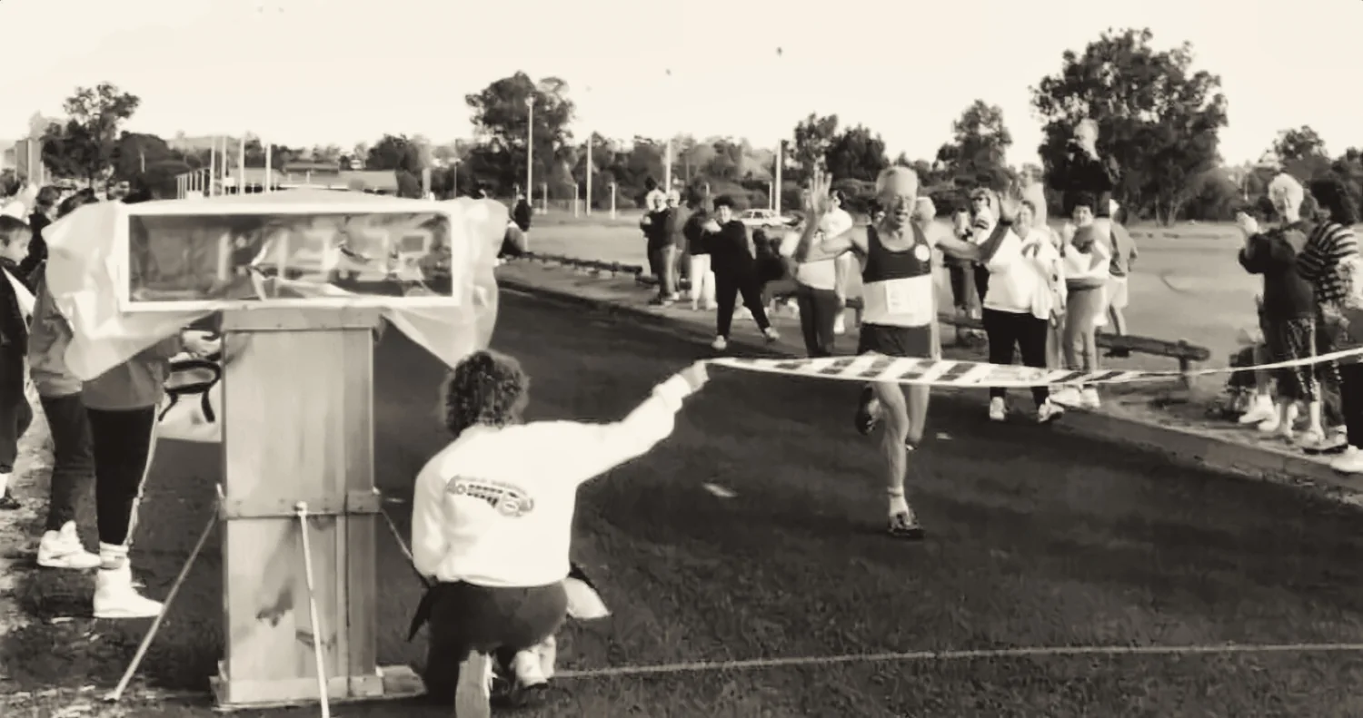 A volunteer crouched at the finish line holding the tape out across the road as a runner approaches.