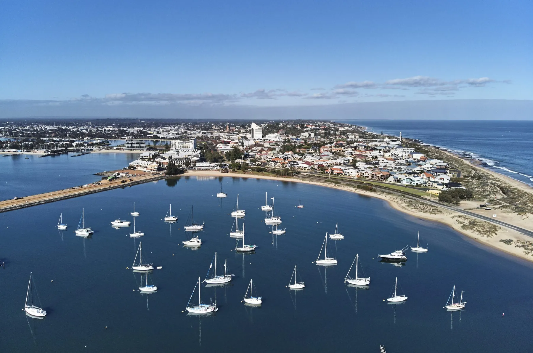 Aerial view over Koombana Bay, yachts moored in the foreground and Bunbury's city centre behind, with Koombana Bay on the left, the Leschenault Inlet behind it, the Indian Ocean on the right and the black-and-white lighthouse on Marlston Hill between them.