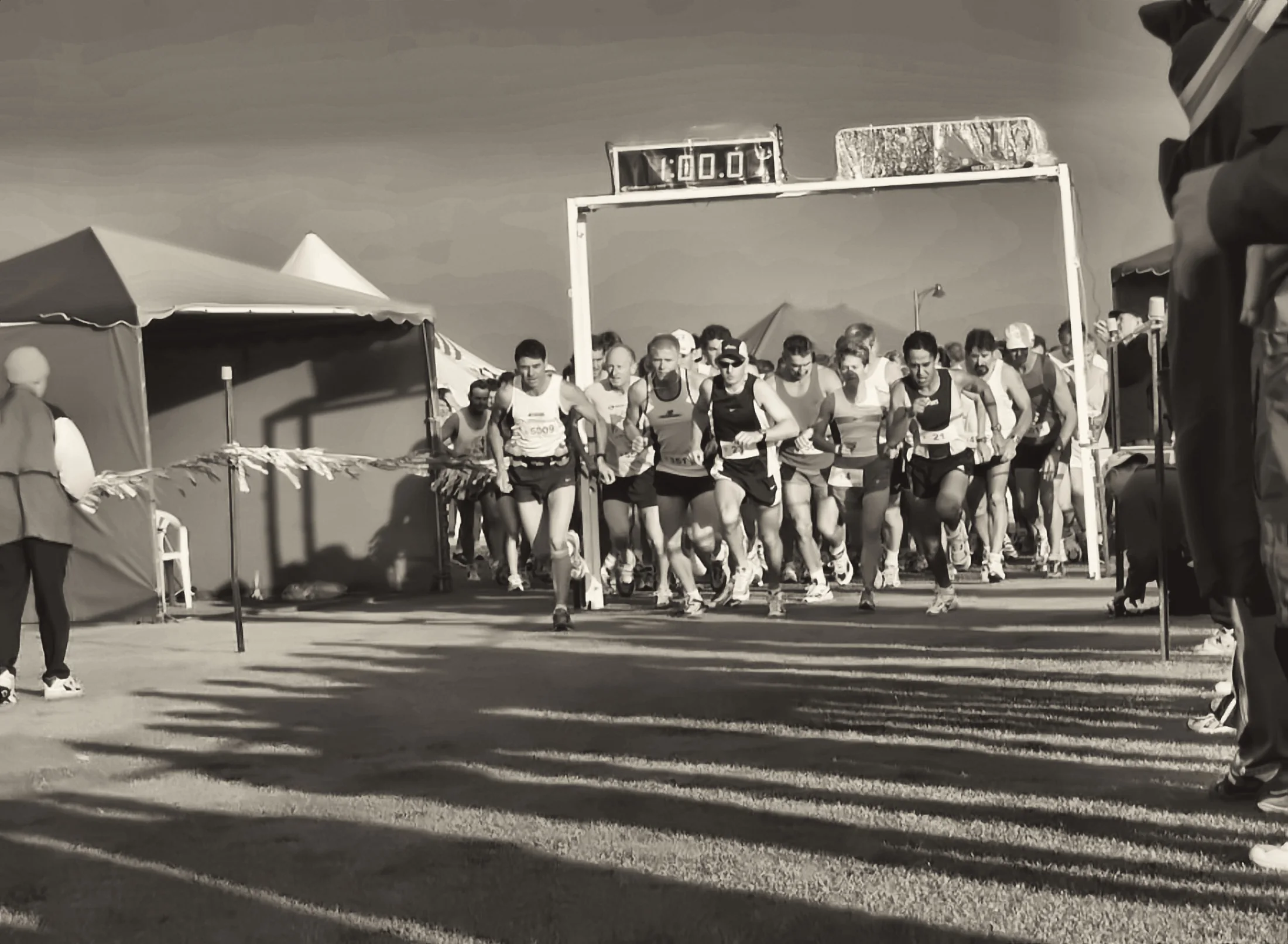 The start line at first light, low sun throwing long shadows across a full field of runners under the race gantry.
