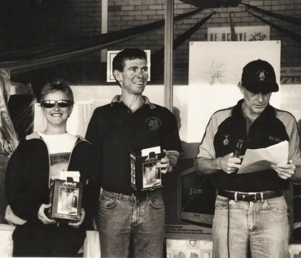 Three people at a presentation holding boxed prizes beneath a Be Active sign.